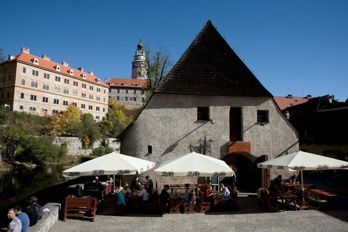 Restaurace ZDROJ — historická budova se štítem nad řekou, v pozadí hradní věž